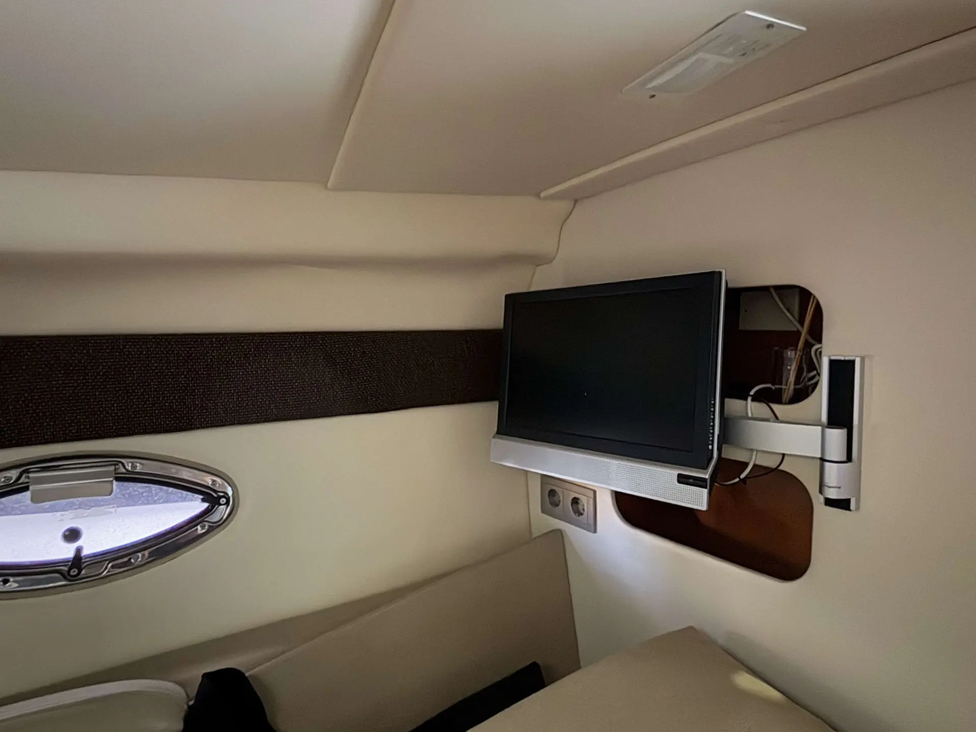 Maxum 2700 — Cabine intérieure avec écran fixé au mur, banquette et hublot.