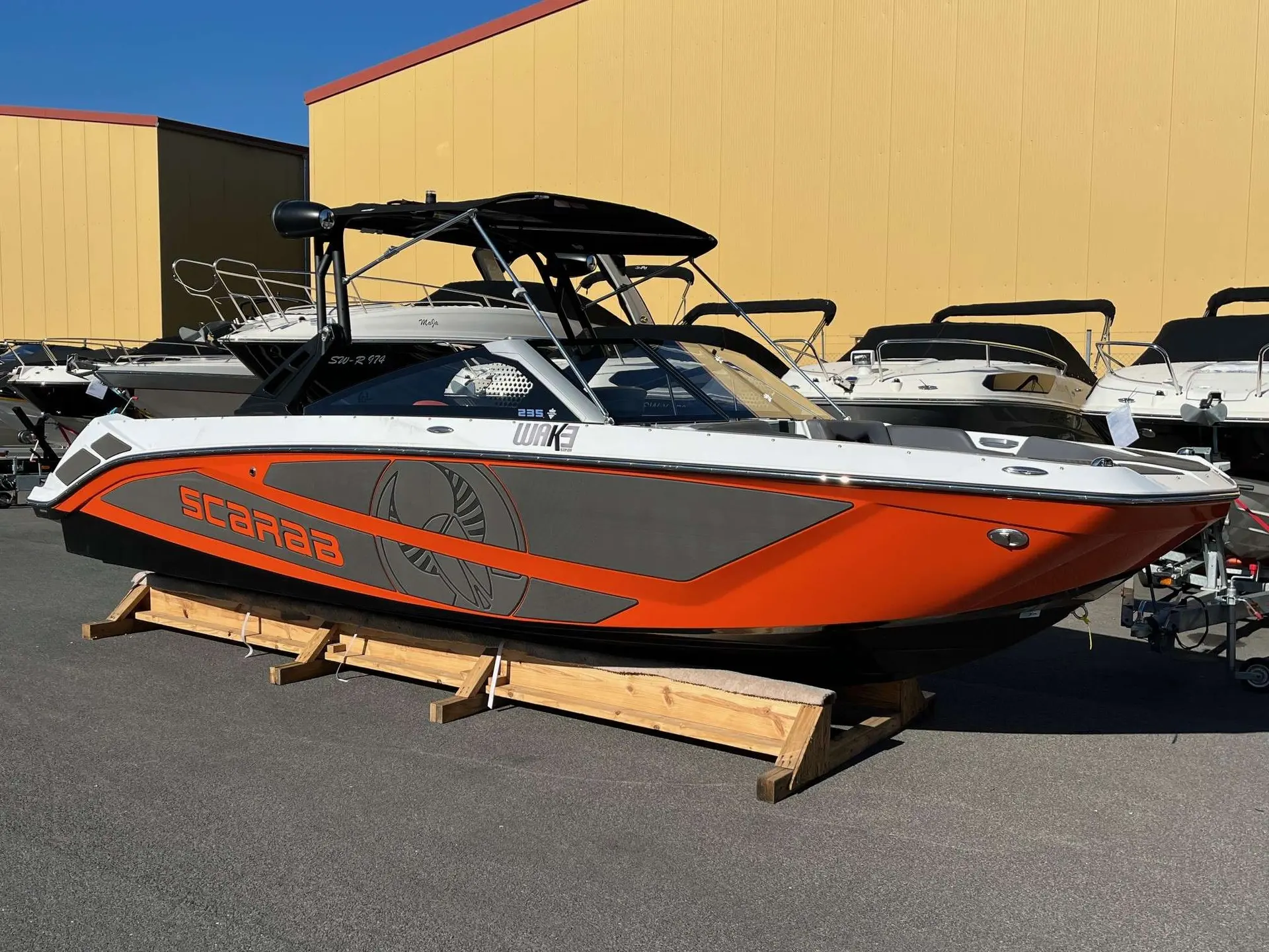 Scarab Boats Scarab — Bateau orange et gris présenté sur berceau, vu de profil dans un parc nautique.