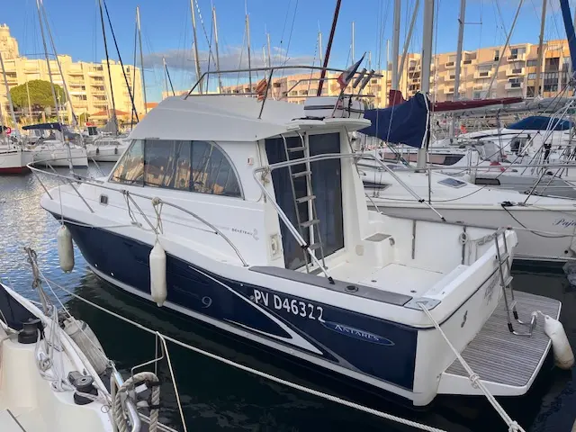 Beneteau Antares Serie 9 — Bateau à moteur blanc et bleu amarré dans une marina, vu de trois quarts arrière.
