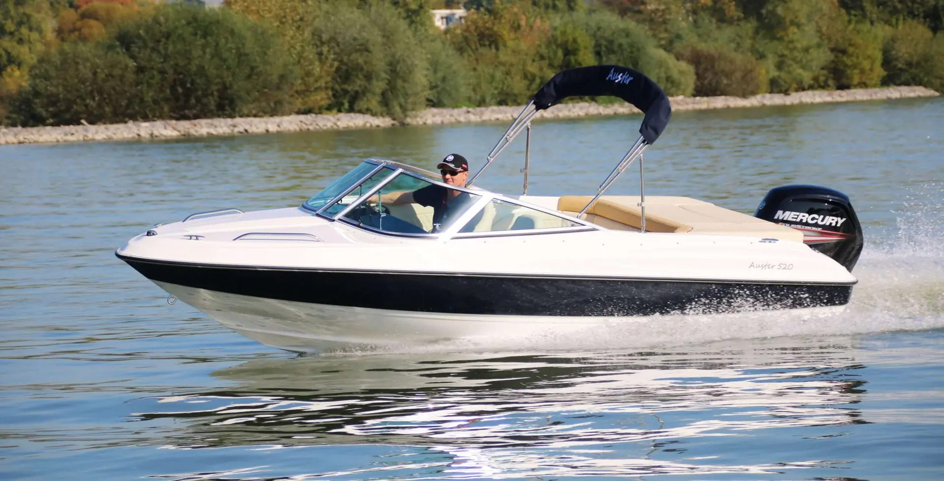 Auster 520 CD — Bateau à moteur blanc et noir naviguant sur un plan d’eau, vu de profil.