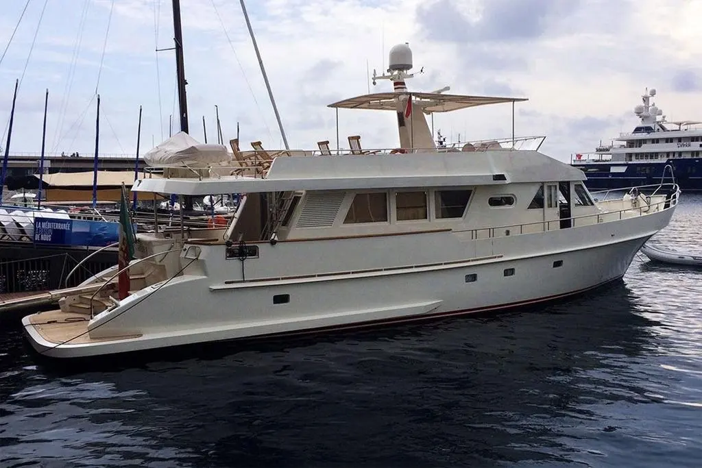Moonen 70 — Yacht à moteur blanc vu de trois-quarts dans un port, amarré parmi d'autres bateaux.