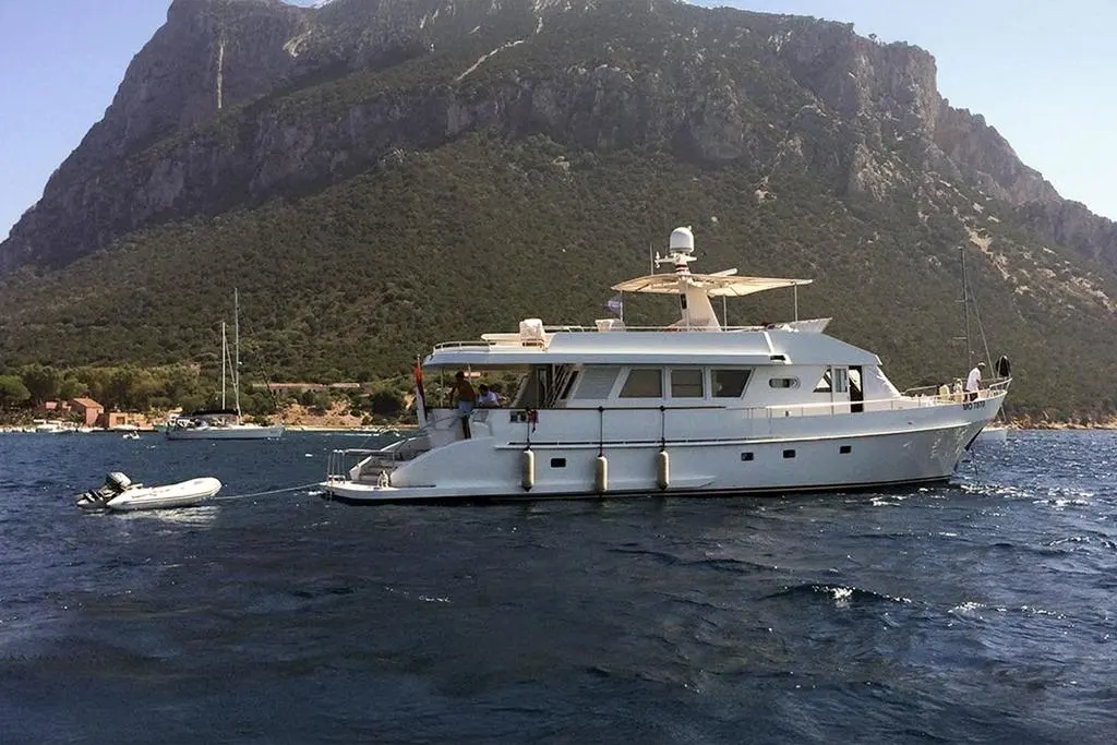 Moonen 70 — Bateau à moteur blanc vu de profil dans une baie, avec une annexe remorquée.