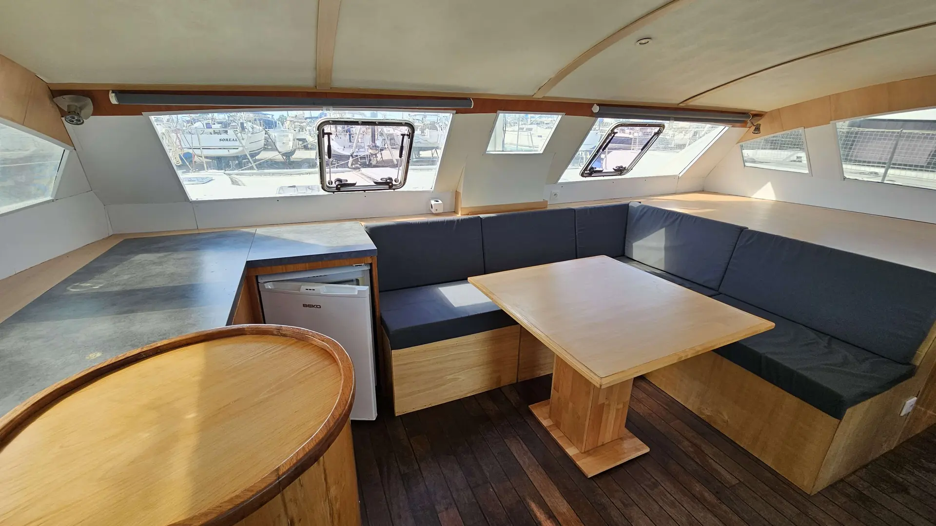 AB Marine Eclipse 472 — Carré intérieur avec banquette en U, table, cuisine et nombreuses fenêtres.