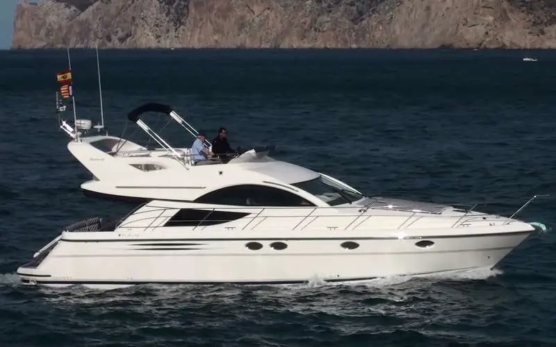 Fairline Phantom 46 — Bateau à moteur blanc vu de profil sur une mer calme, avec deux personnes à bord.