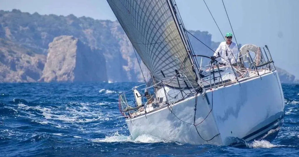 Grand Soleil 44 — Voilier blanc naviguant au près dans une mer agitée, avec des falaises en arrière-plan.