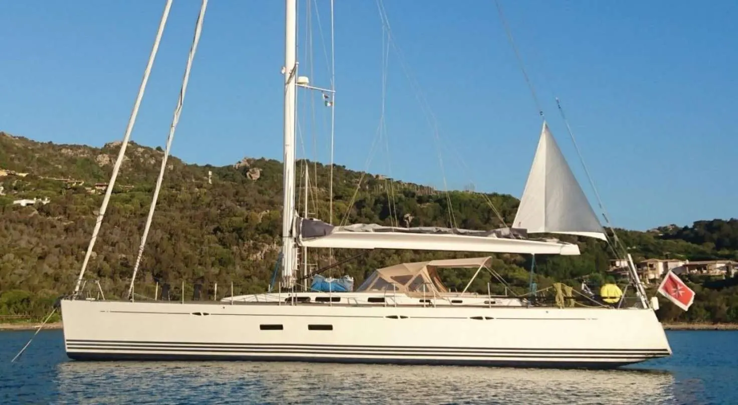 X-Yachts X-65 — Voilier blanc vu de profil, amarré sur une eau calme devant une côte boisée.