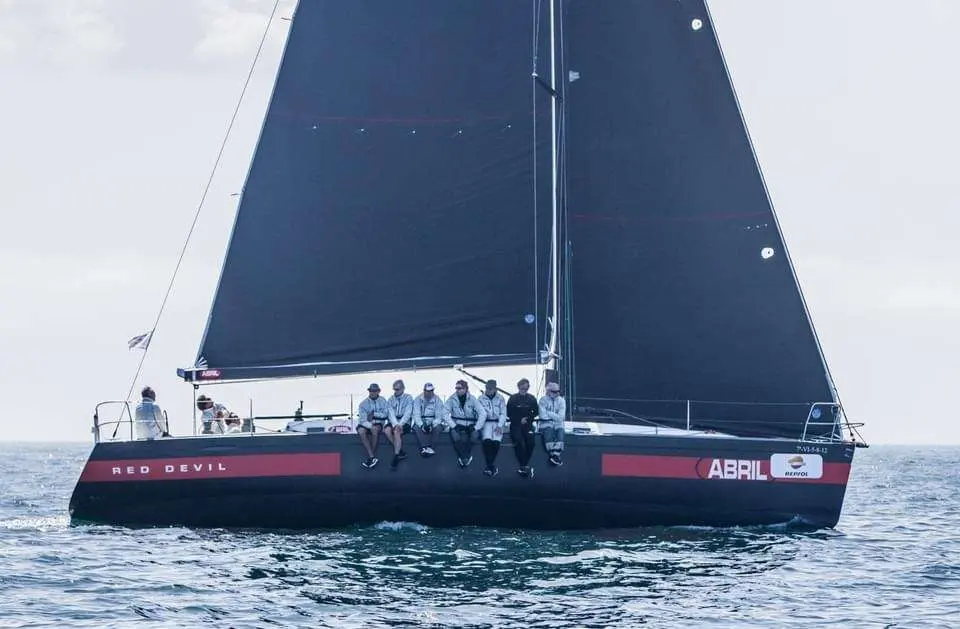 Beneteau First 44.7 — Voilier de course noir et rouge naviguant en mer, avec plusieurs personnes à bord.