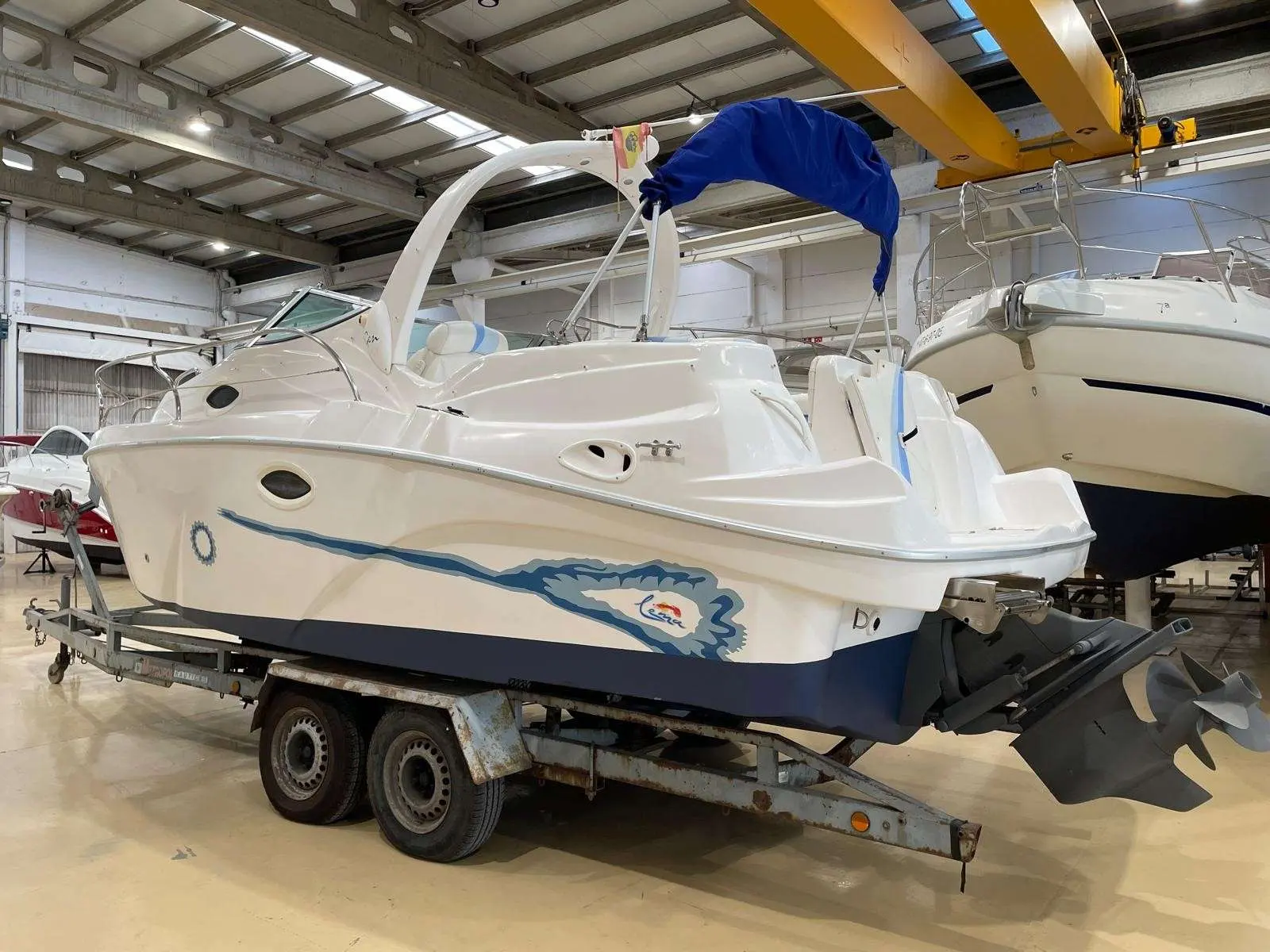 Lema Gen — Bateau à moteur blanc vu de trois quarts arrière dans un hangar, sur remorque.