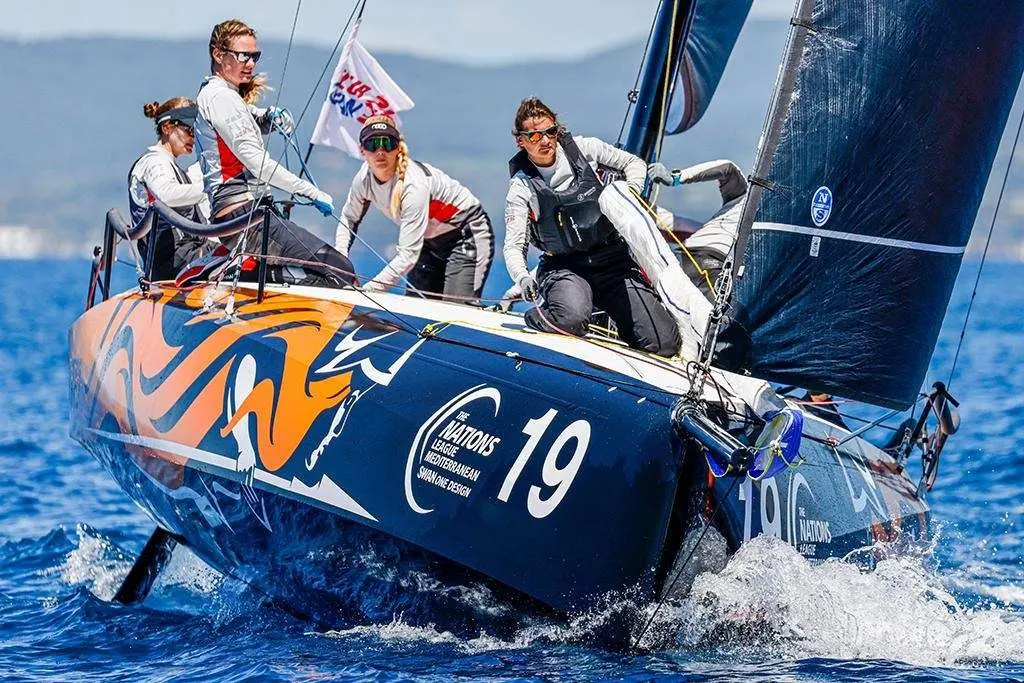Nautor Swan Swan 36 — Voilier de course bleu et orange naviguant au près avec quatre équipiers à bord.