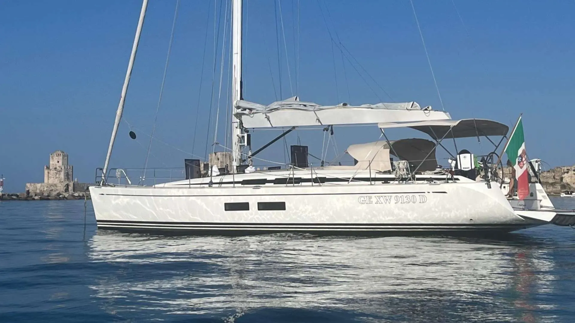 Nautor Swan Swan 54 — Voilier blanc vu de profil sur l’eau, avec château côtier en arrière-plan.