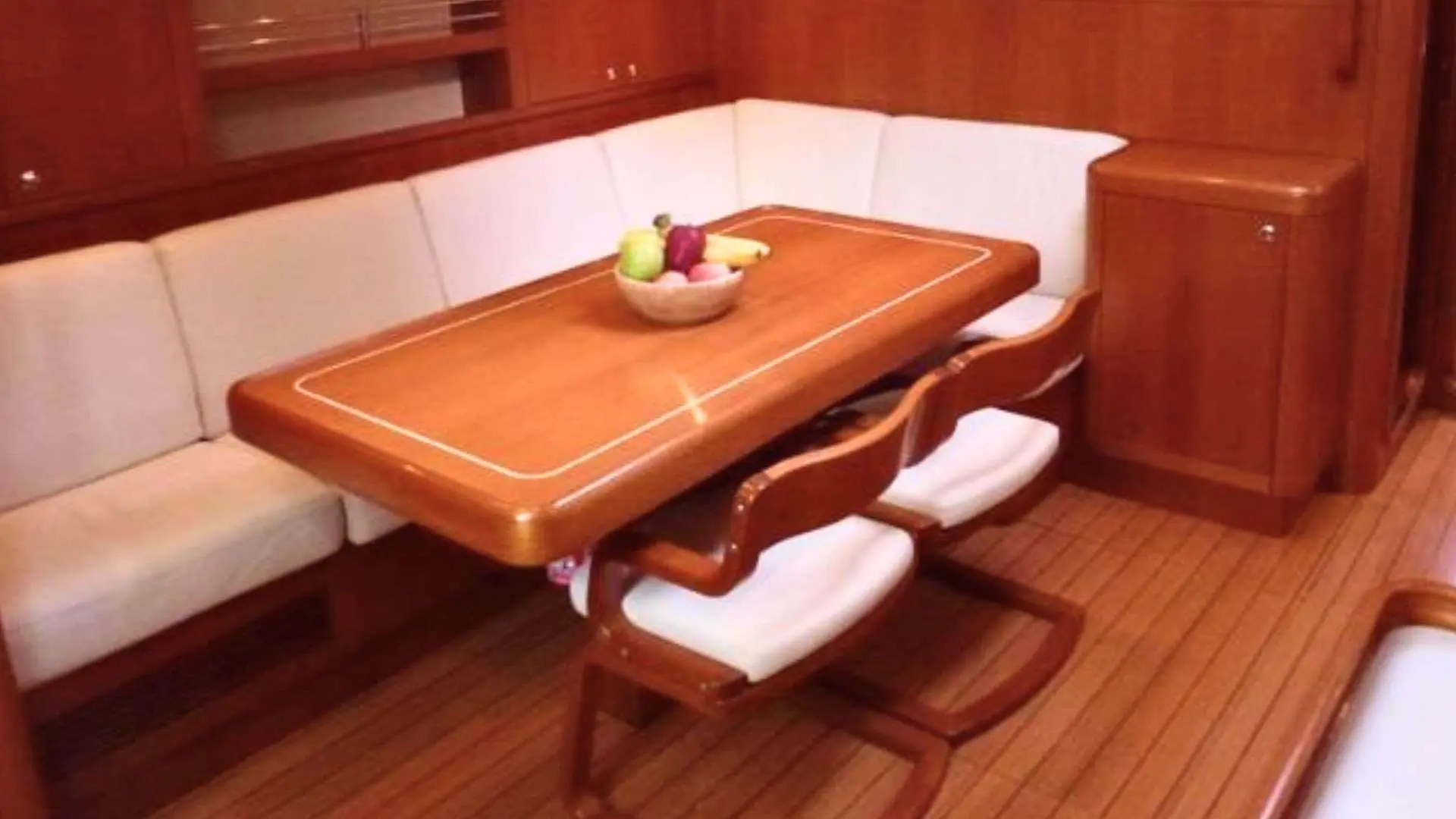 Nautor Swan Swan 53 — Carré intérieur en bois avec banquette, table et fauteuils rembourrés.