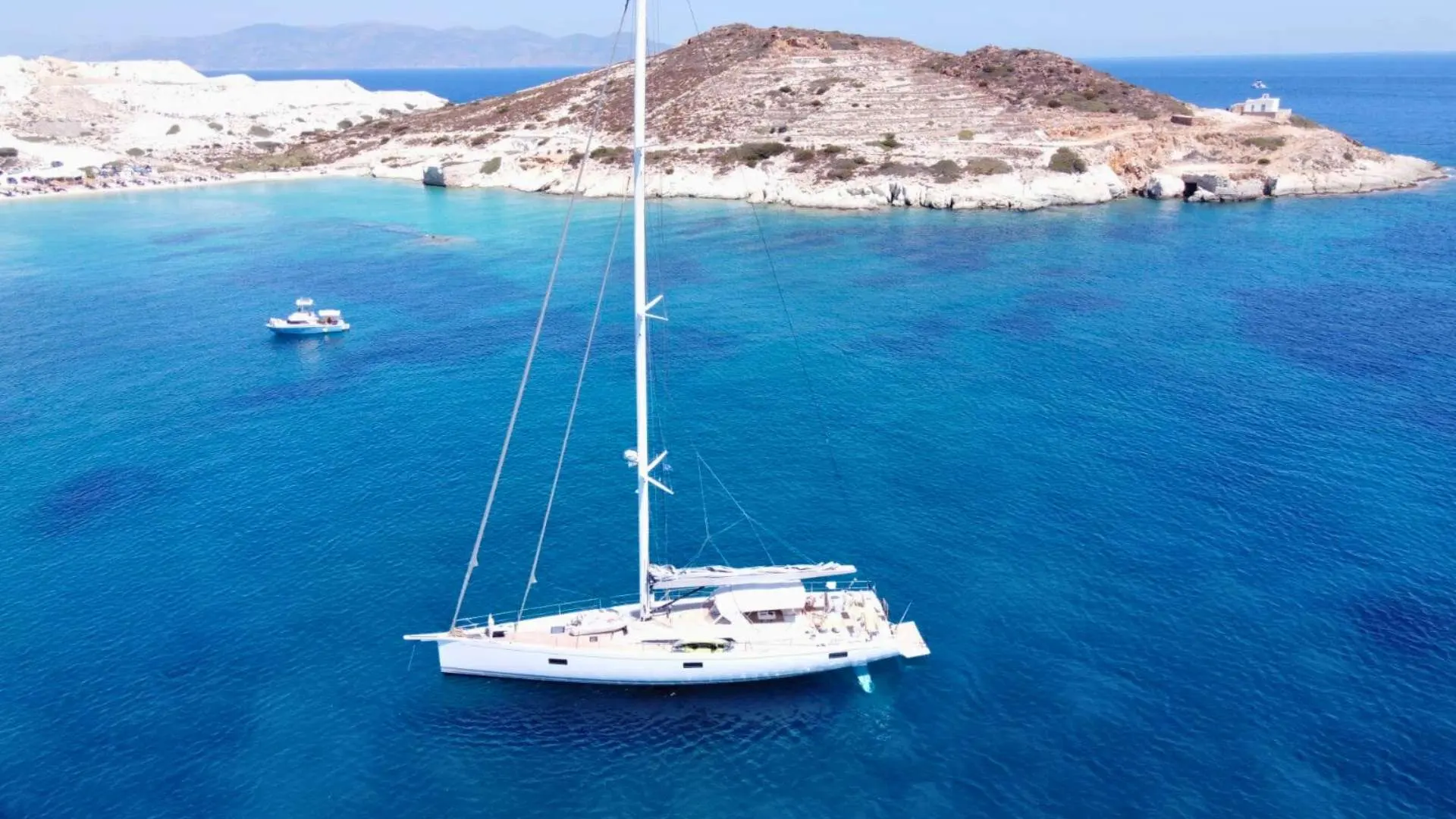 Nautor Swan Swan 78 — Voilier blanc vu de trois quarts au mouillage devant une côte rocheuse.