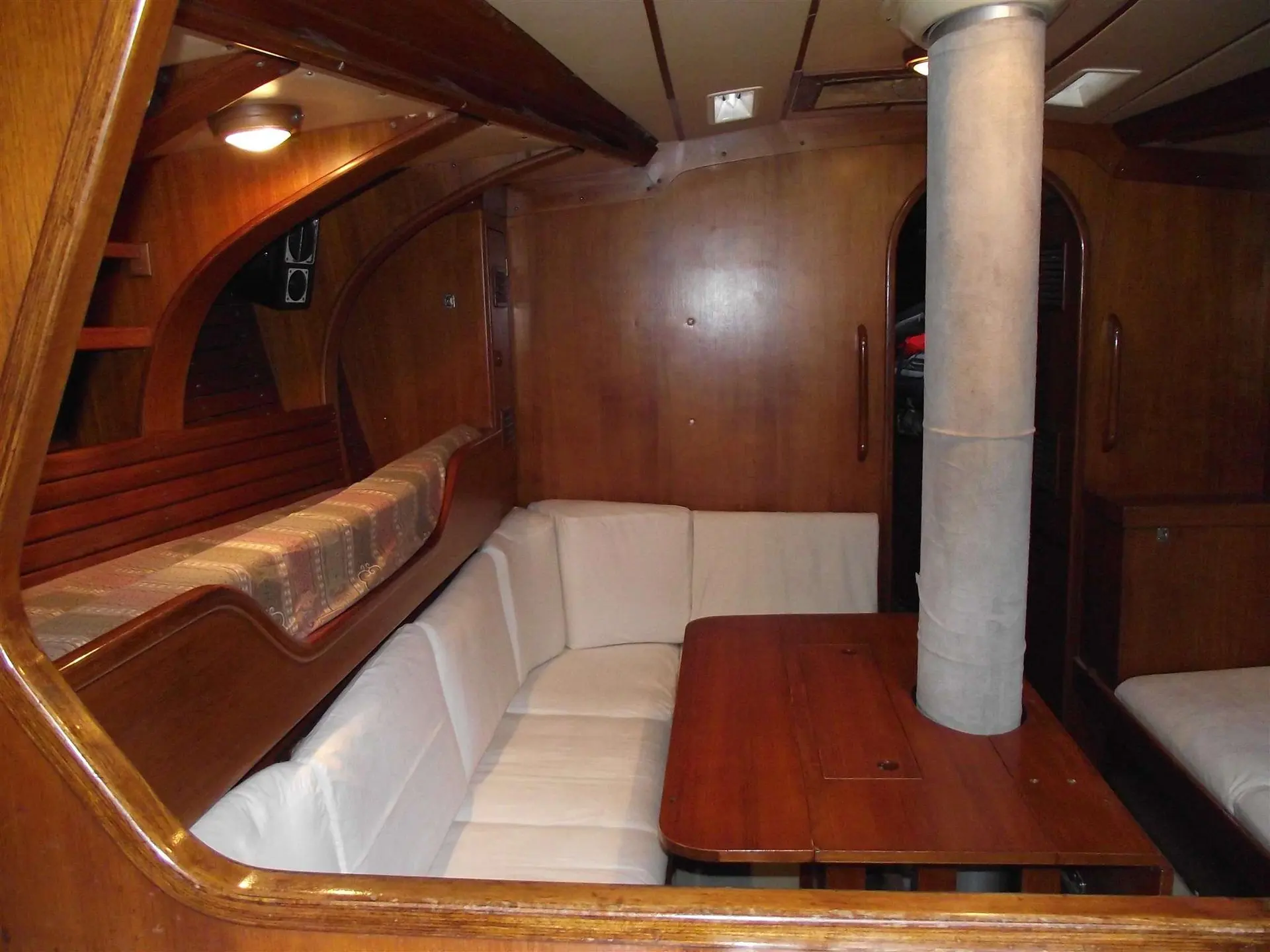 Nautor Swan Swan 47 — Vue du carré intérieur en bois, avec banquettes, table et mât apparent.
