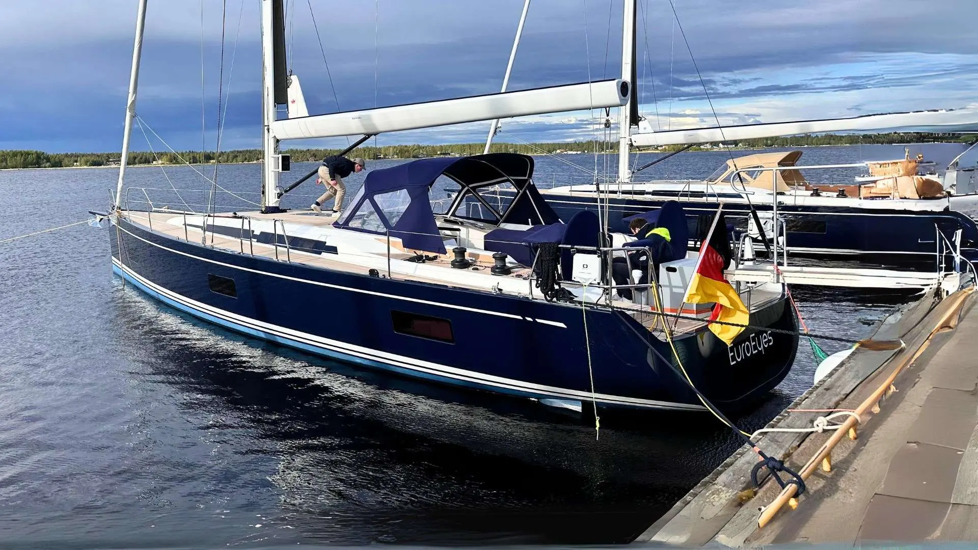 Nautor Swan Swan 55 — Voilier bleu amarré au quai, avec deux personnes et d’autres bateaux en arrière-plan.