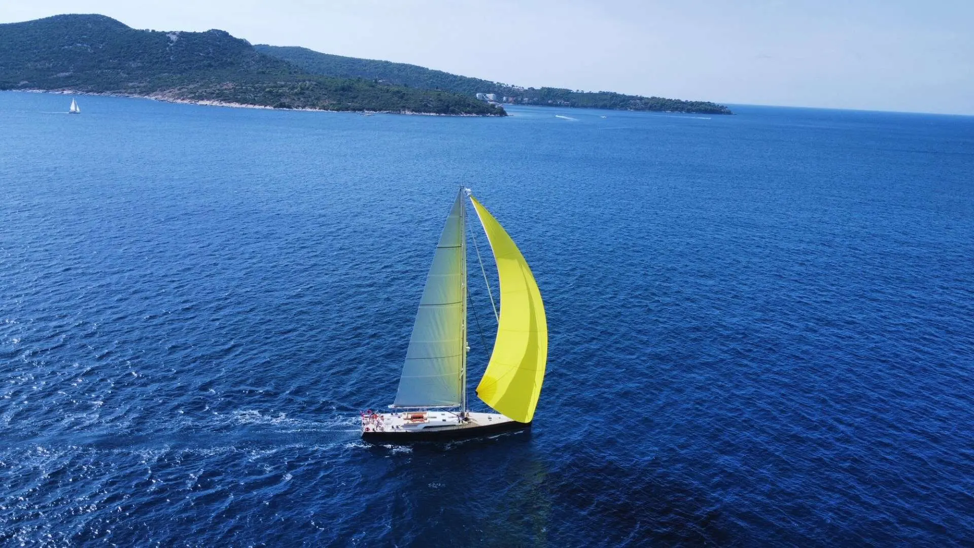 Nautor Swan Swan 98 — Voilier vu du ciel, naviguant au large avec une voile d’avant jaune.