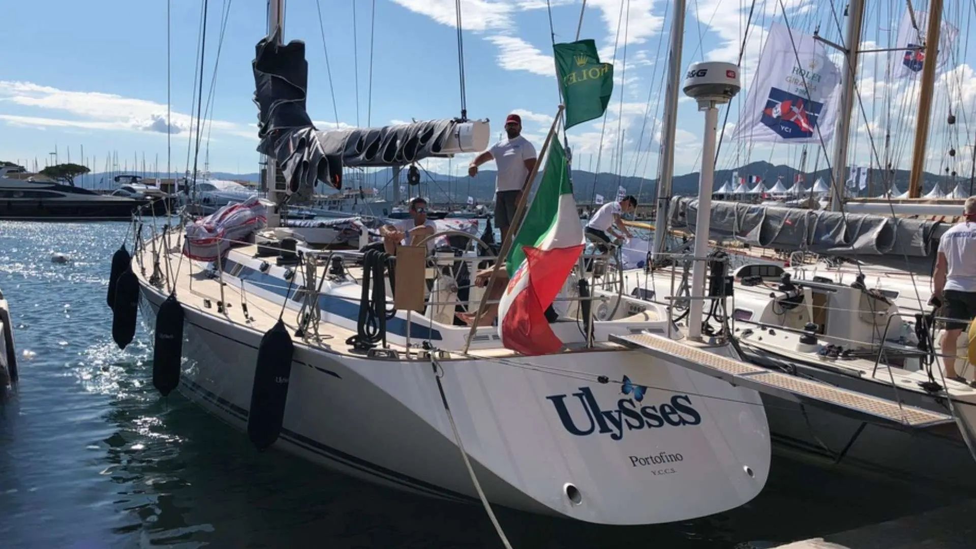 Nautor Swan Swan 60 — Voilier blanc vu de trois quarts arrière dans un port, avec plusieurs personnes à bord.