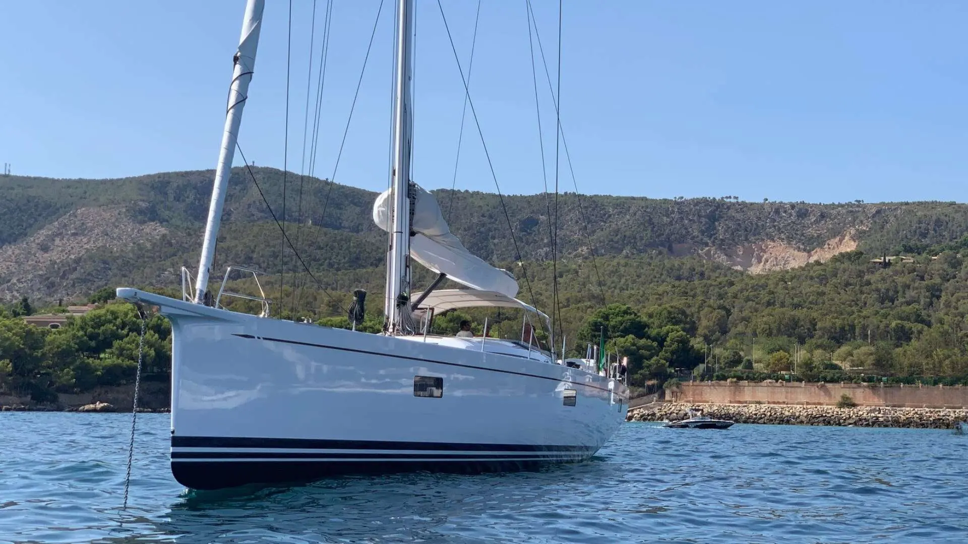 Nautor Swan Swan 78 — Voilier blanc au mouillage, vu de trois quarts, devant une côte boisée.