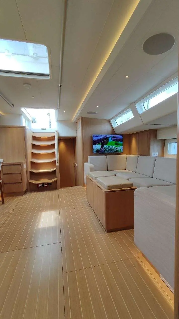 Nautor Swan Swan 78 — Salon intérieur lumineux avec canapé d’angle, télévision et rangements en bois.