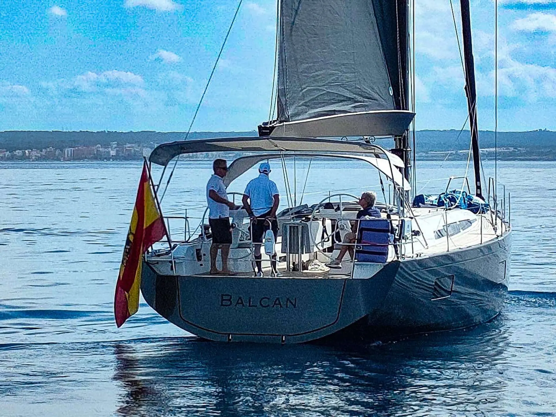 Nautor Swan Swan 48 — Voilier vu de trois-quarts arrière, toutes voiles hissées, avec trois personnes à bord.