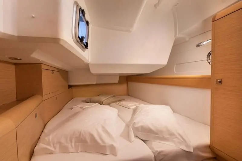 Jeanneau Sun Odyssey 479 — Cabine avec couchette double, rangements en bois et hublot latéral.