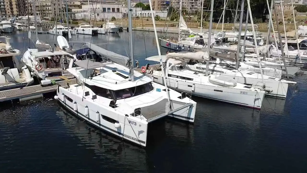 Fountaine Pajot Lucia 40 — Catamaran blanc vu de trois-quarts amarré dans une marina.