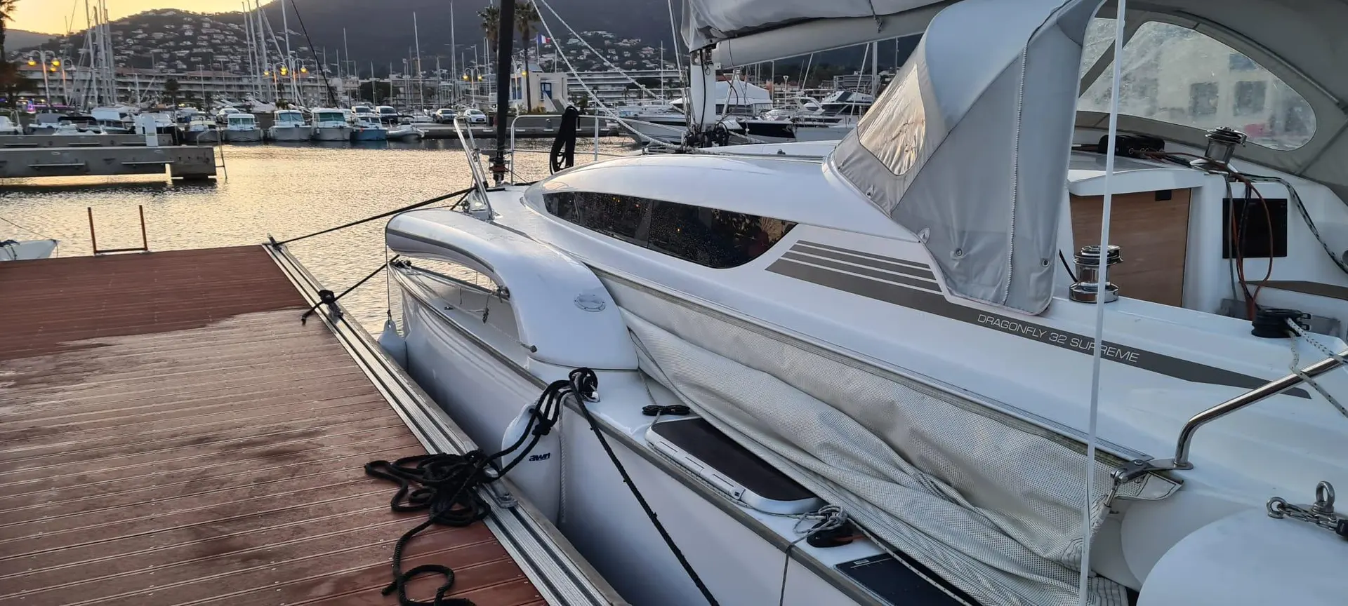 Dragonfly 32 — Trimaran blanc amarré dans une marina au coucher du soleil.