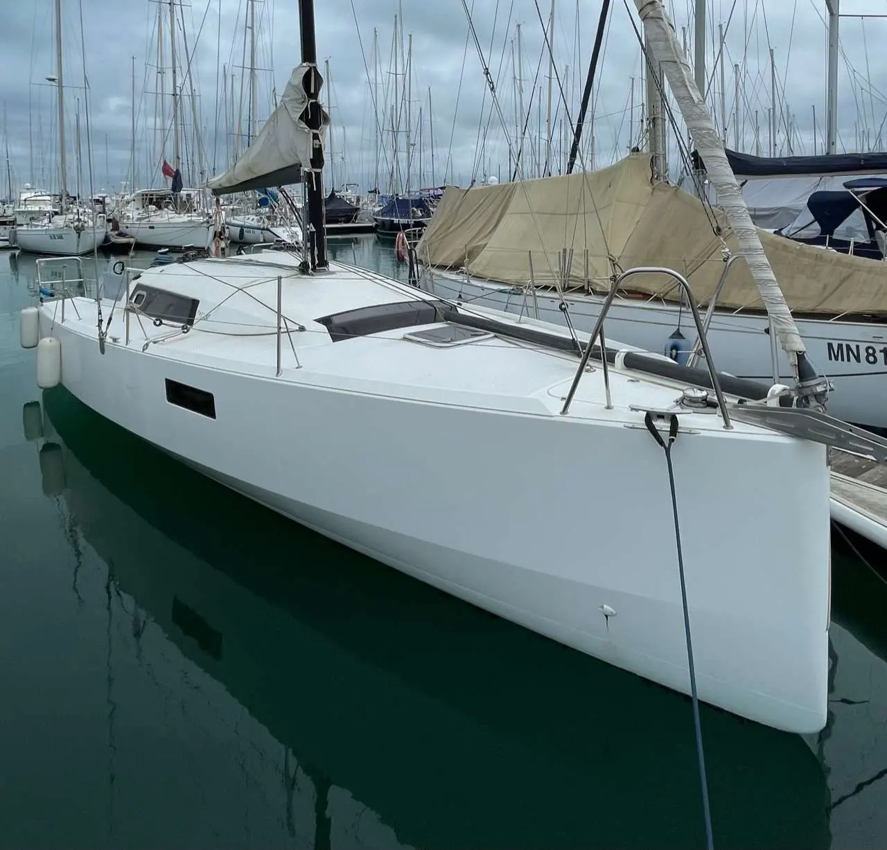 Pogo Structures Pogo 30 — Voilier blanc vu de trois quarts avant, amarré dans un port parmi d’autres bateaux.