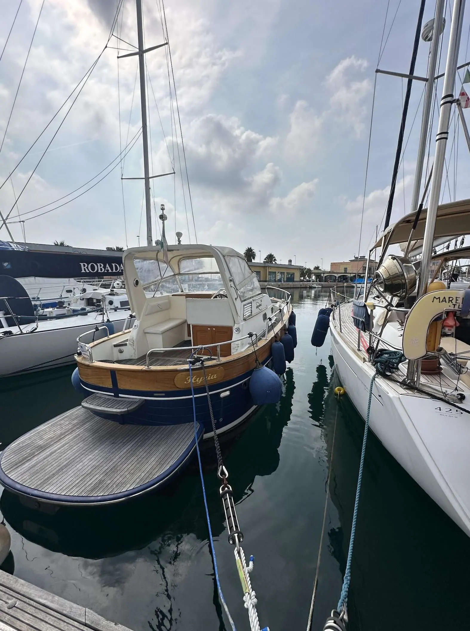 Apreamare 28 Semi Cabinato — Bateau amarré vu de poupe dans un port, entre deux autres embarcations.