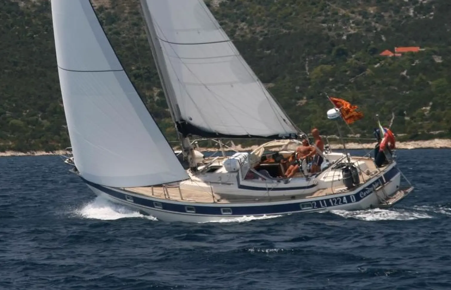 Hallberg Rassy 38 — Voilier naviguant sous voiles près d’une côte boisée.