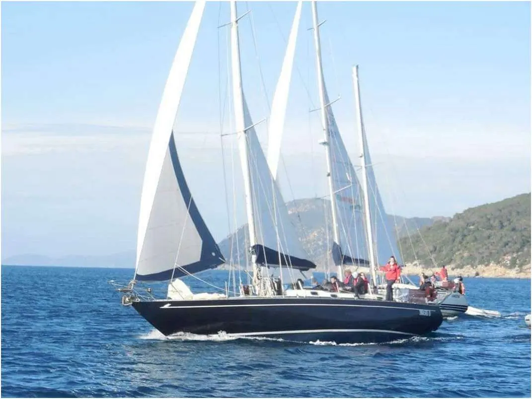 RPD Cidivino Nelson 46 — Voilier noir naviguant sous voiles près d’une côte rocheuse.
