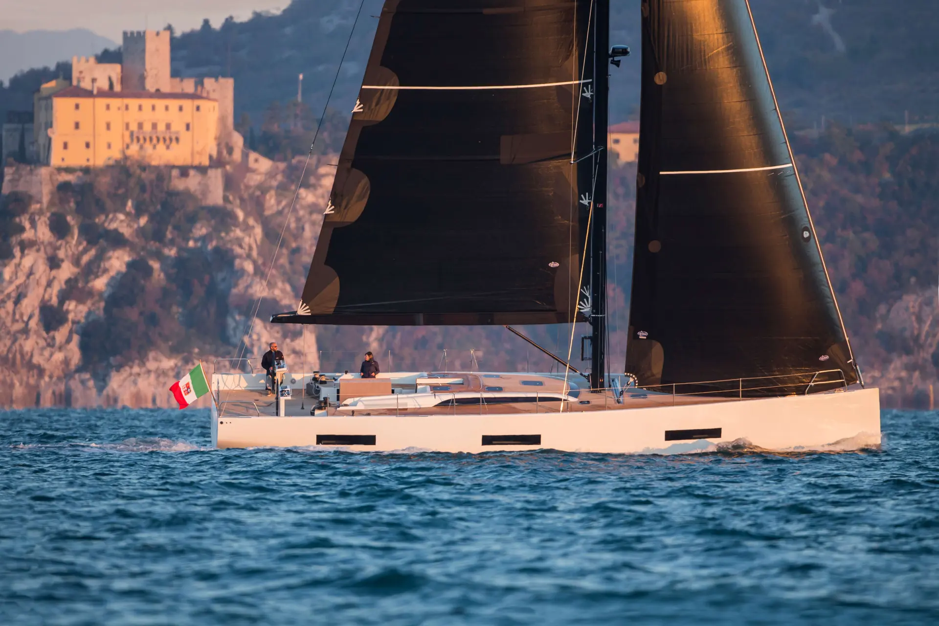 Solaris 60 — Voilier vu de profil sous voiles, naviguant devant une forteresse côtière.