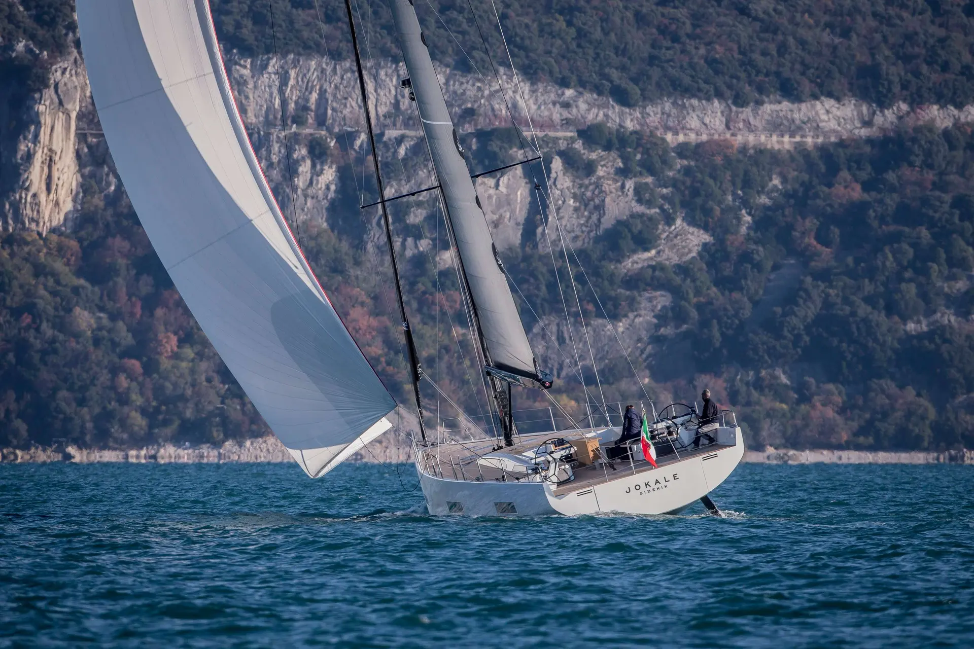 Solaris 60 — Voilier blanc sous voiles au large d'une côte rocheuse.