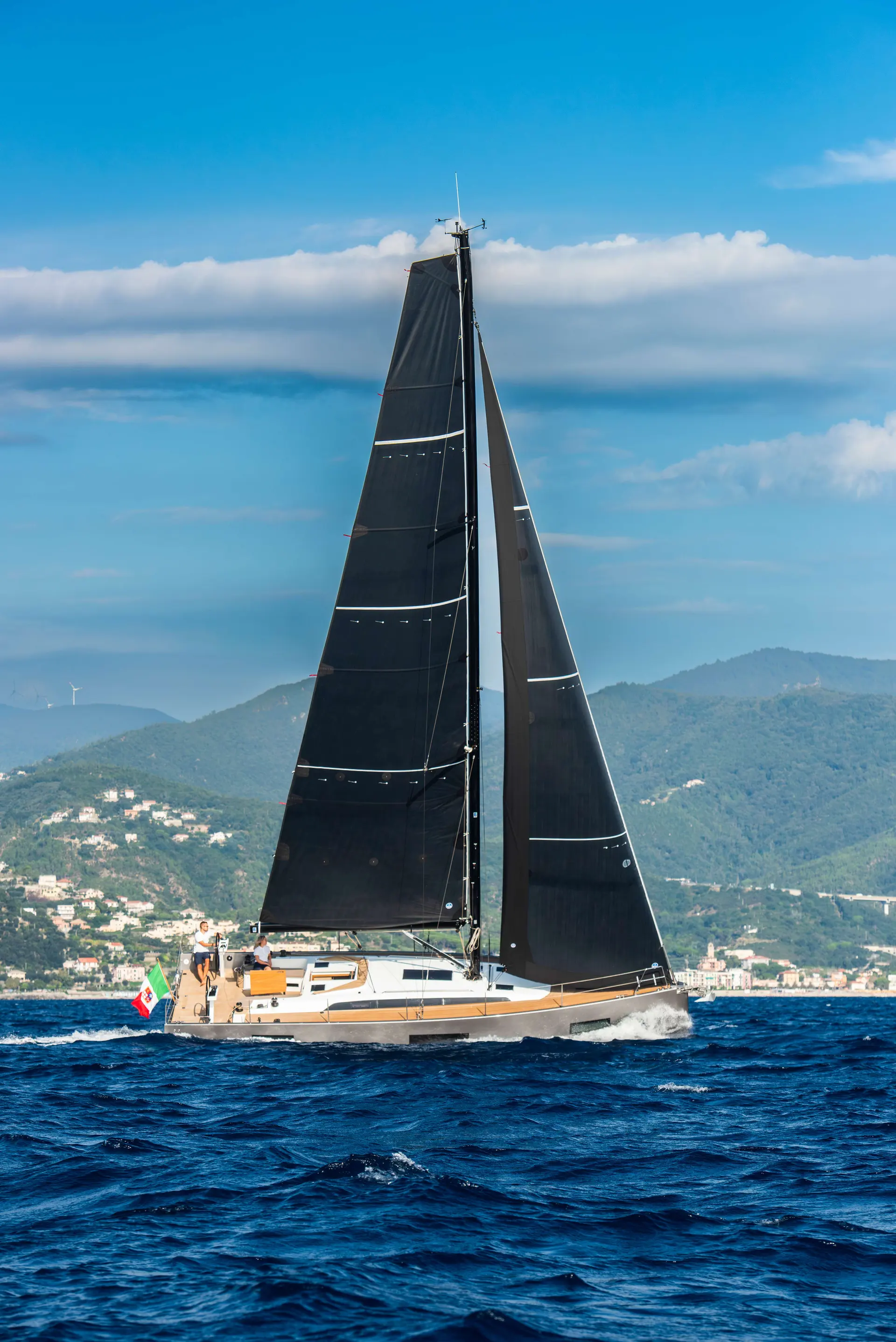 Solaris 40 ST — Voilier aux voiles noires naviguant près d'une côte montagneuse.