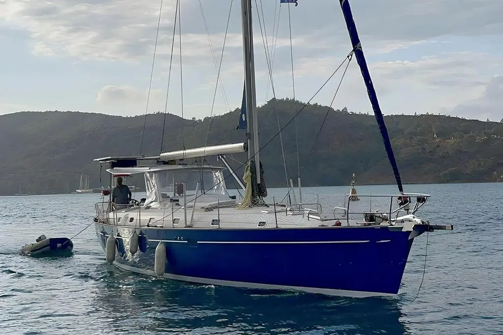 Beneteau 50 — Voilier bleu et blanc vu de trois quarts dans une baie, avec annexe à bâbord.