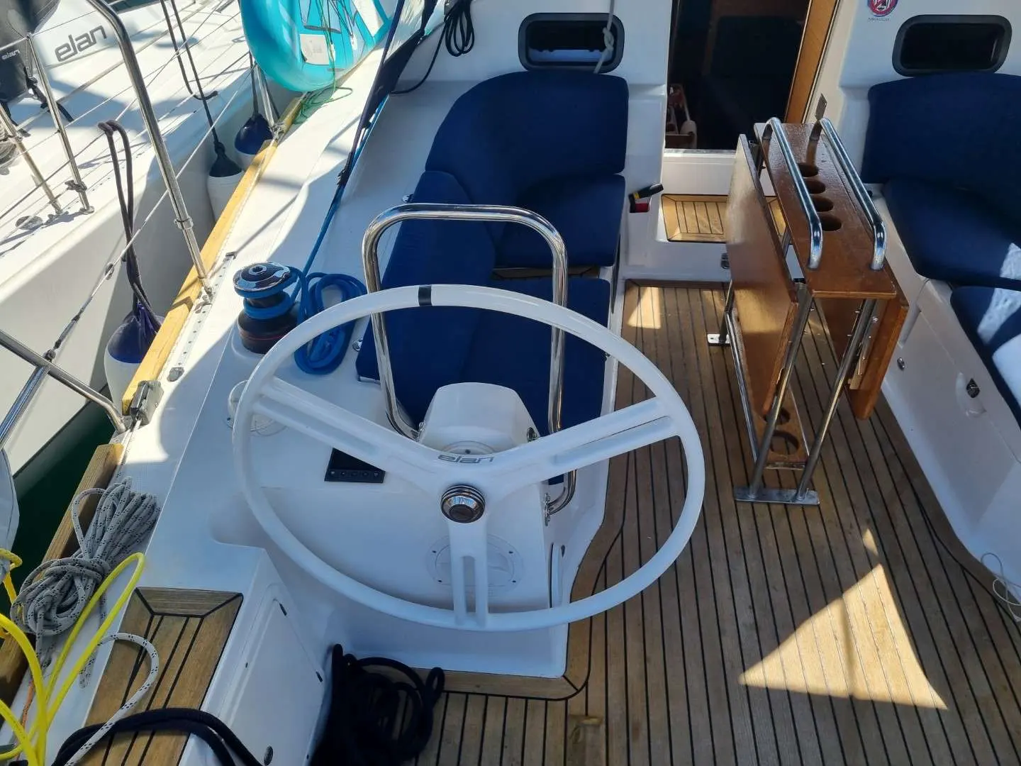 Elan Impression 40 — Vue du cockpit d’un voilier, avec barre à roue, sièges et pont en teck.