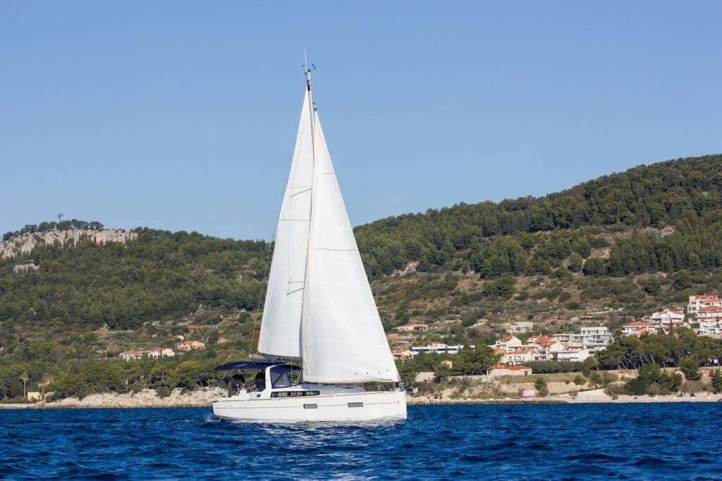 Beneteau Oceanis 38 — Voilier blanc naviguant près d’une côte boisée, toutes voiles hissées.