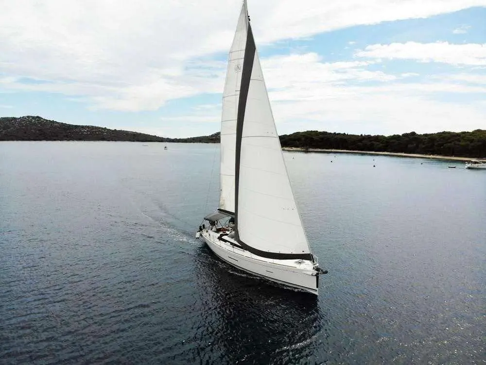 Dufour 450 — Voilier blanc vu de trois quarts, toutes voiles hissées dans une baie abritée.