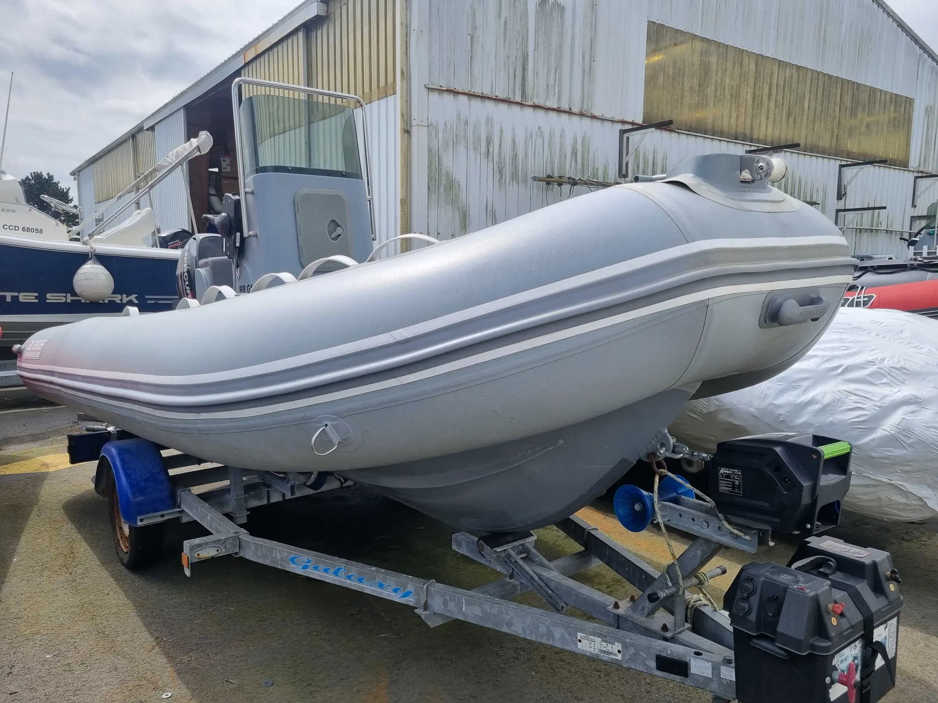 3D Tender Stealth RIB 500 — Bateau pneumatique gris sur remorque, photographié devant un hangar.