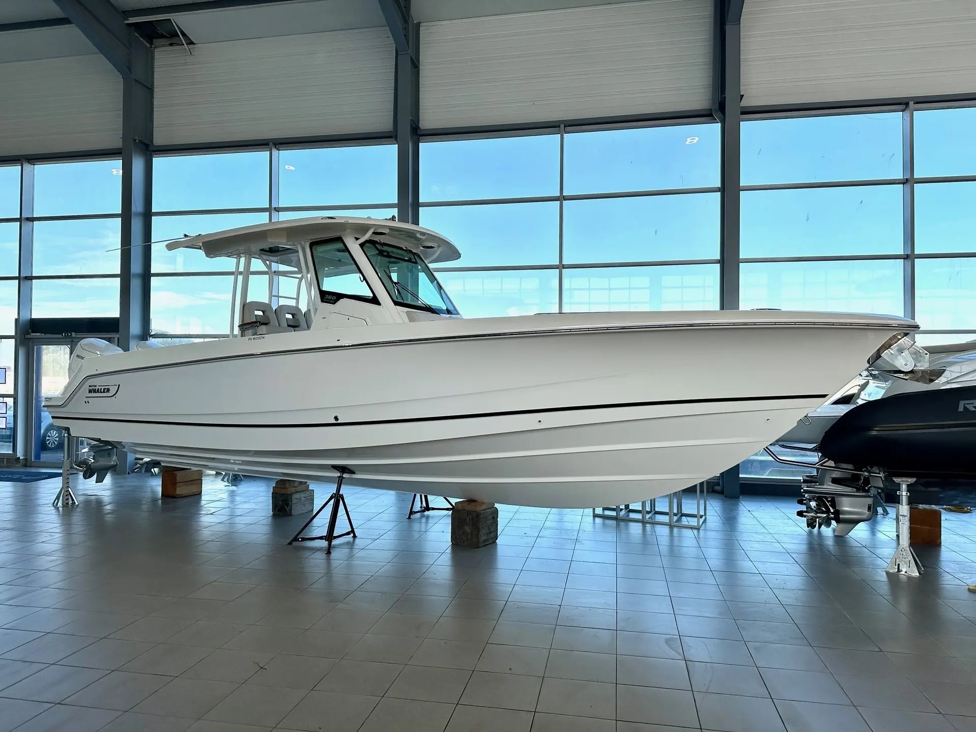 Boston Whaler 360 Outrage — Bateau blanc à console centrale présenté sur bers dans un showroom vitré.
