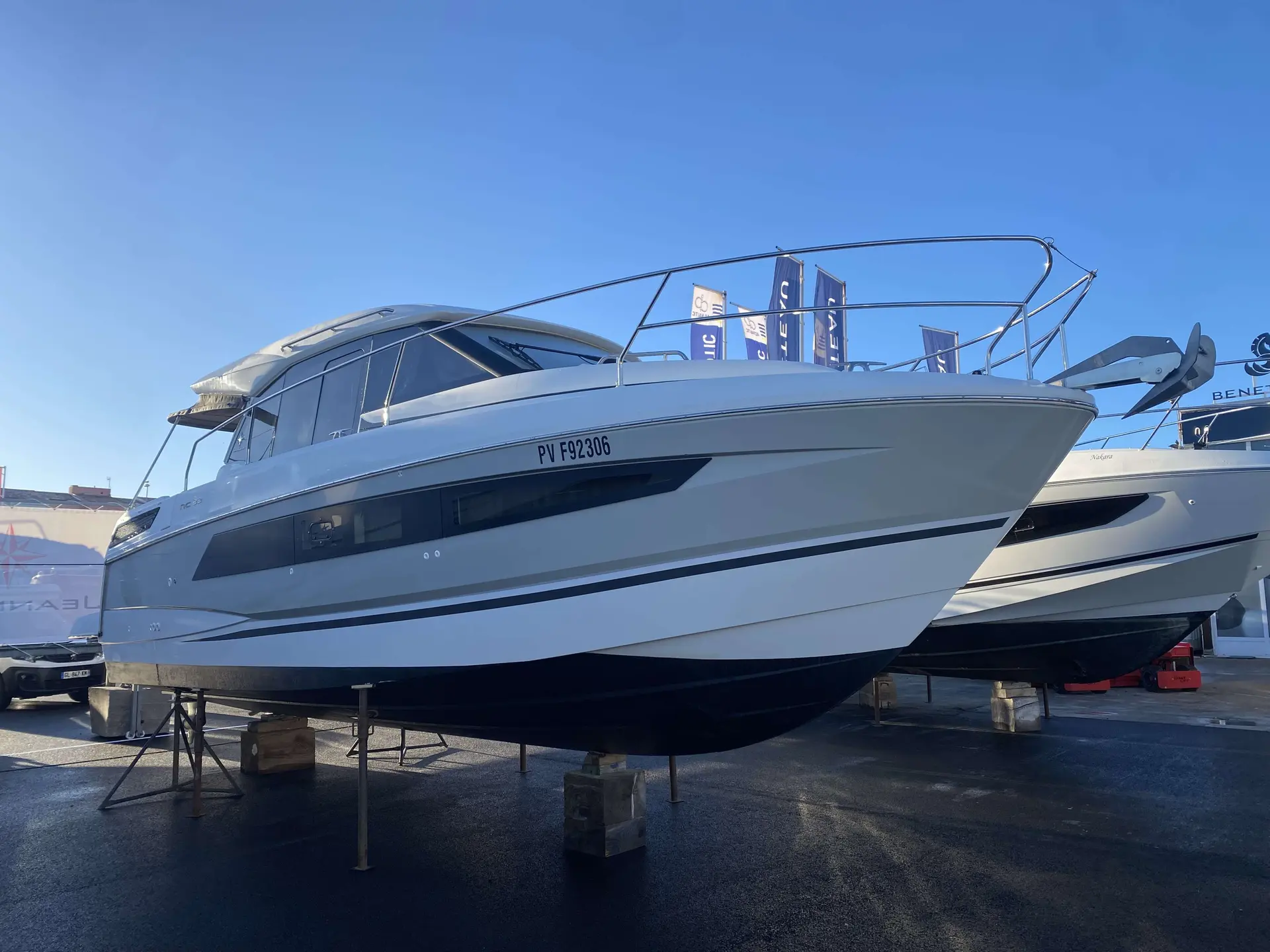 Jeanneau NC 33 — Bateau à moteur blanc exposé sur bers, photographié de trois quarts avant.