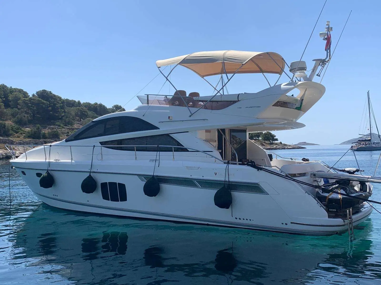 Fairline Phantom 48 — Bateau à moteur blanc vu de trois quarts, au mouillage dans une baie.