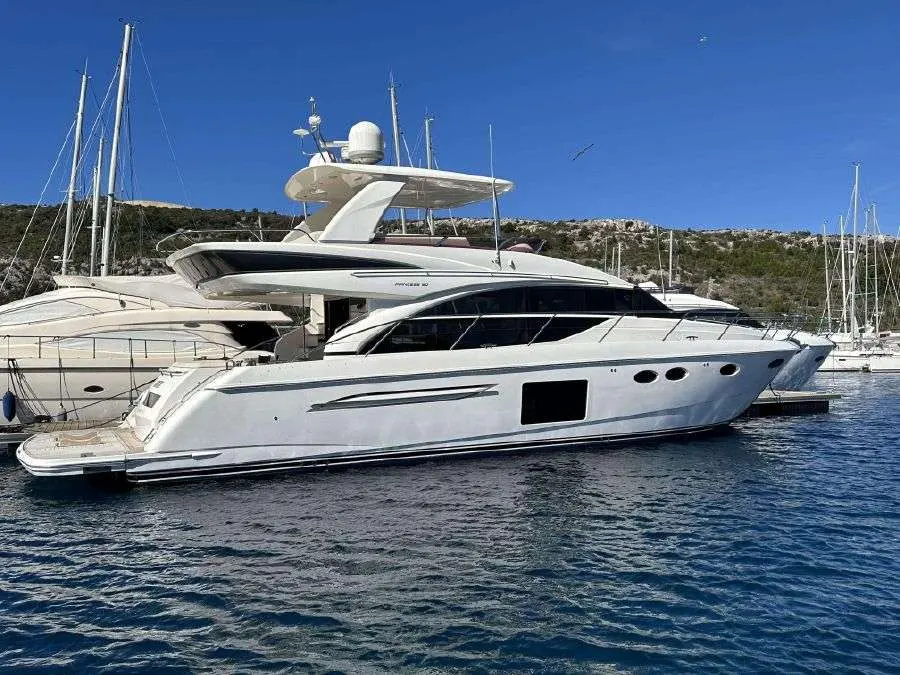 Princess 60 Fly — Bateau à moteur blanc vu de profil dans une marina, avec des voiliers en arrière-plan.