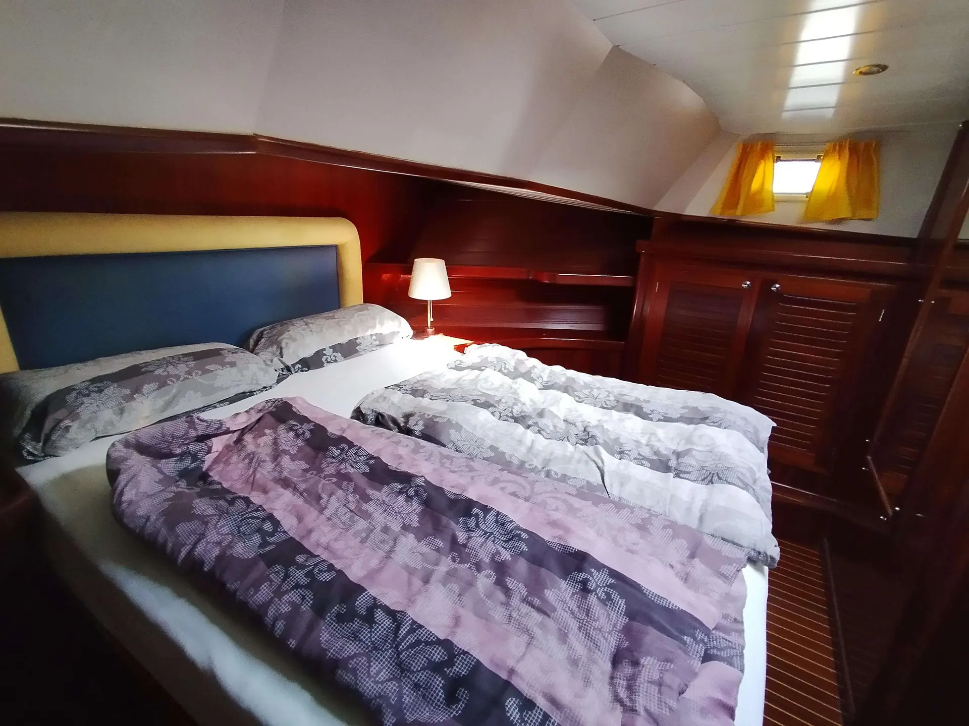 Menorquin 150 — Cabine avec lit double, boiseries et fenêtre à rideaux jaunes.