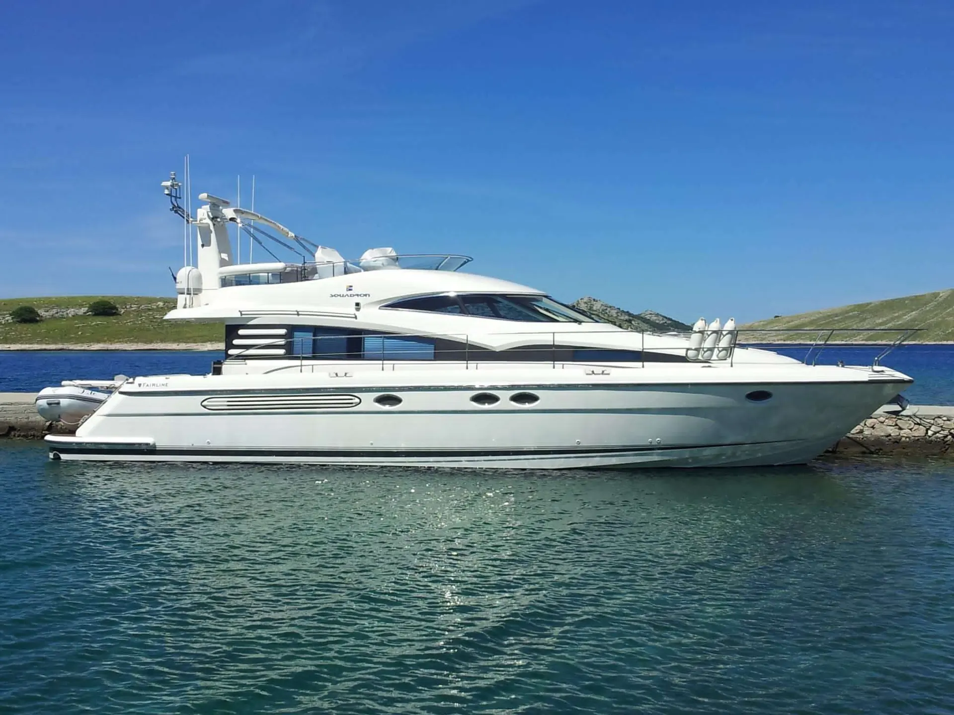 Fairline Squadron 52 — Bateau à moteur blanc vu de profil, amarré dans une baie aux eaux turquoise.