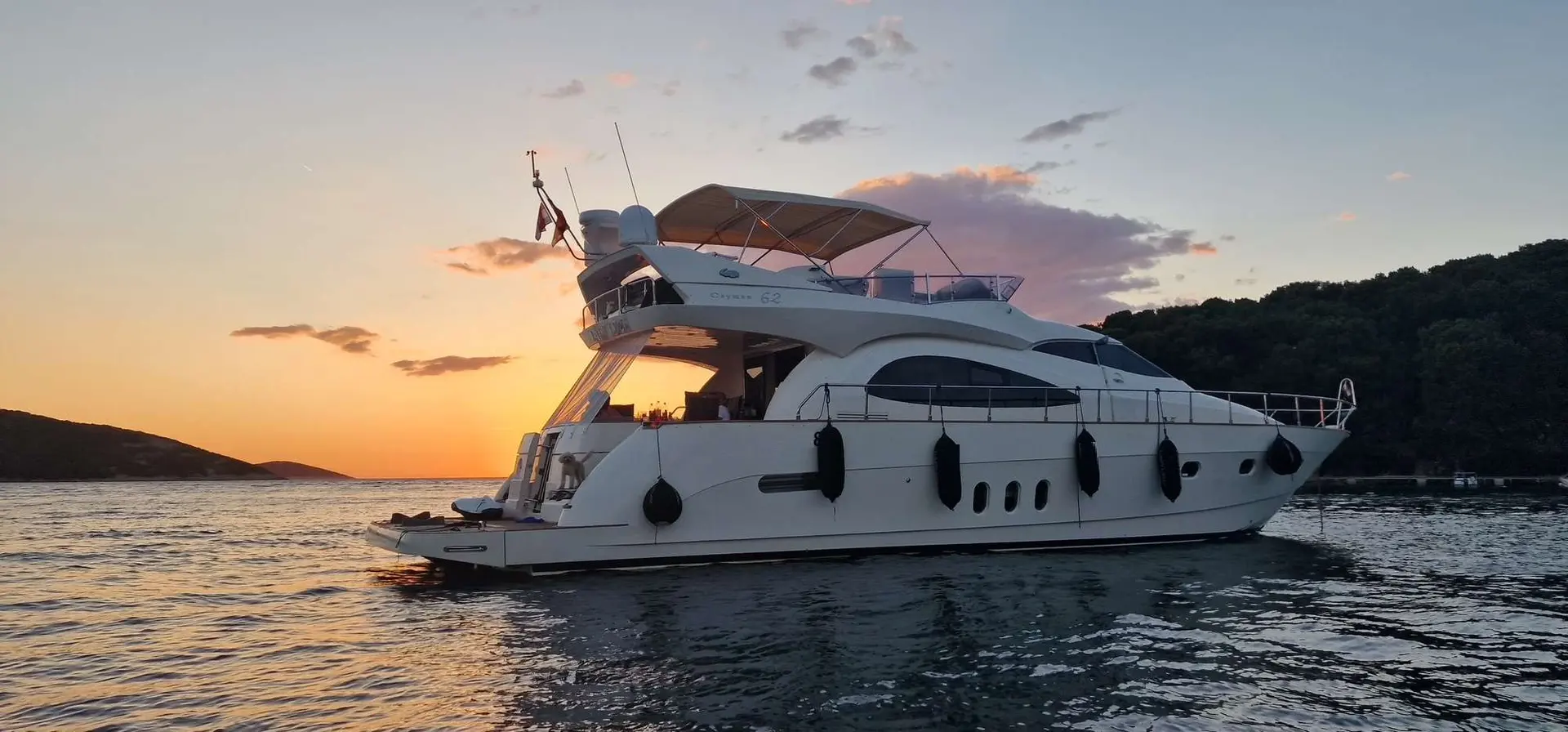 Cayman 62 Fly — Yacht à moteur blanc photographié de profil sur l’eau au coucher du soleil.