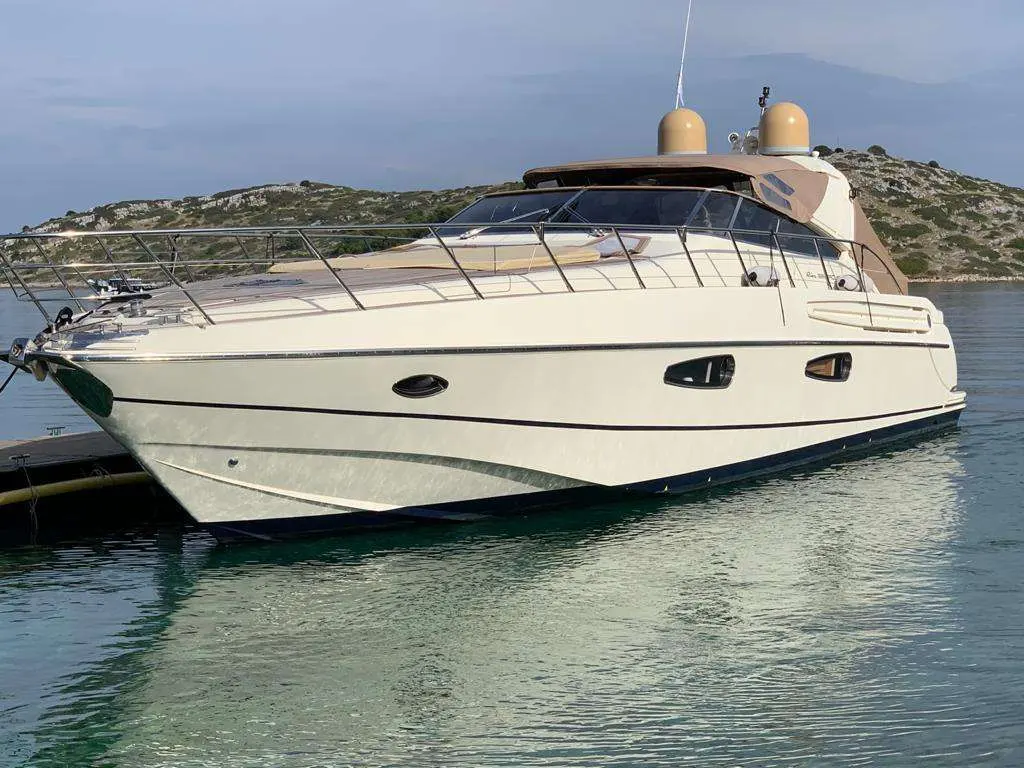 Riva Mercurius 59 — Bateau à moteur vu de trois quarts, amarré devant une côte rocheuse.