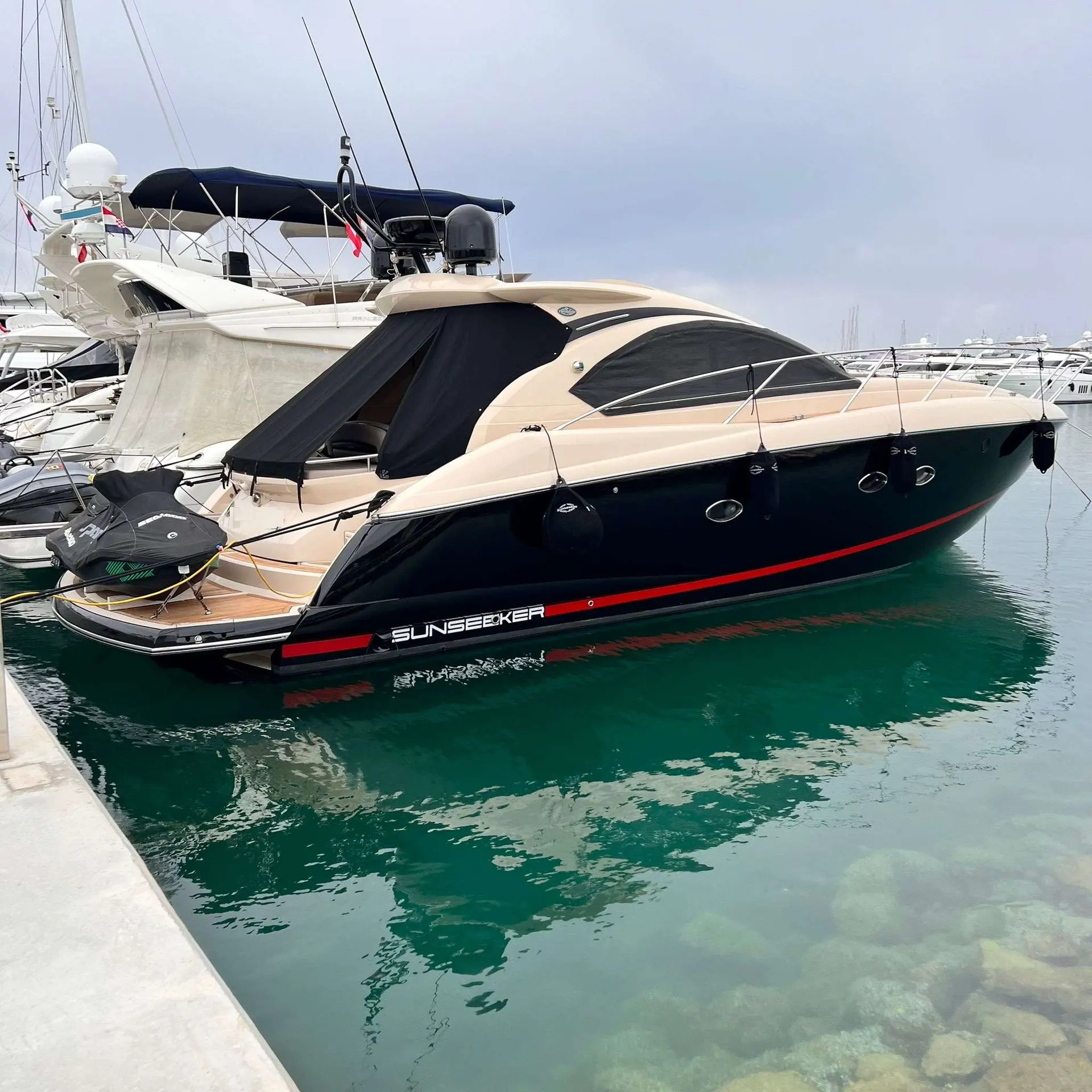 Sunseeker Portofino 47 — Bateau à moteur noir et crème amarré dans un port, vu de trois quarts arrière.