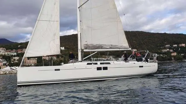Hanse 505 — Voilier blanc vu de profil, toutes voiles hissées, naviguant près d'une côte habitée.