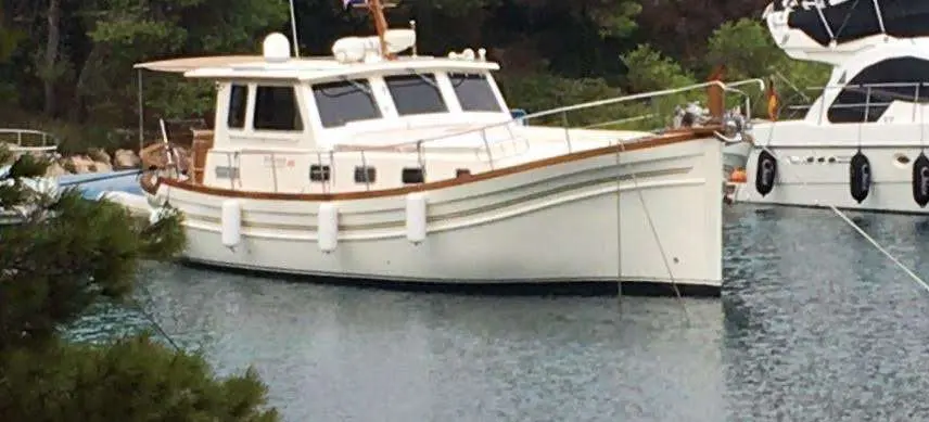 Menorquin 160 — Bateau à moteur blanc vu de trois quarts dans un port, entre des bateaux amarrés.