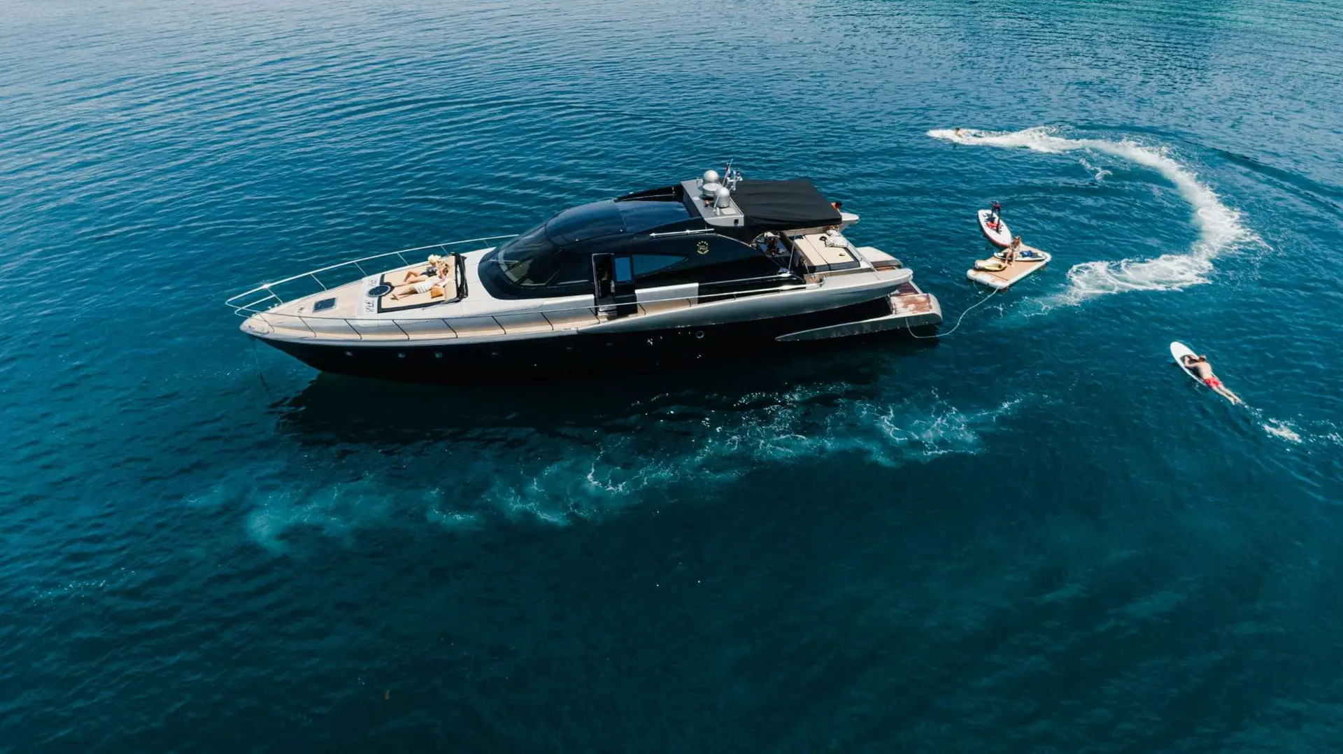 Fashion Yachts Fashion 68 — Vue aérienne d’un yacht à moteur noir entouré de personnes sur des engins nautiques.